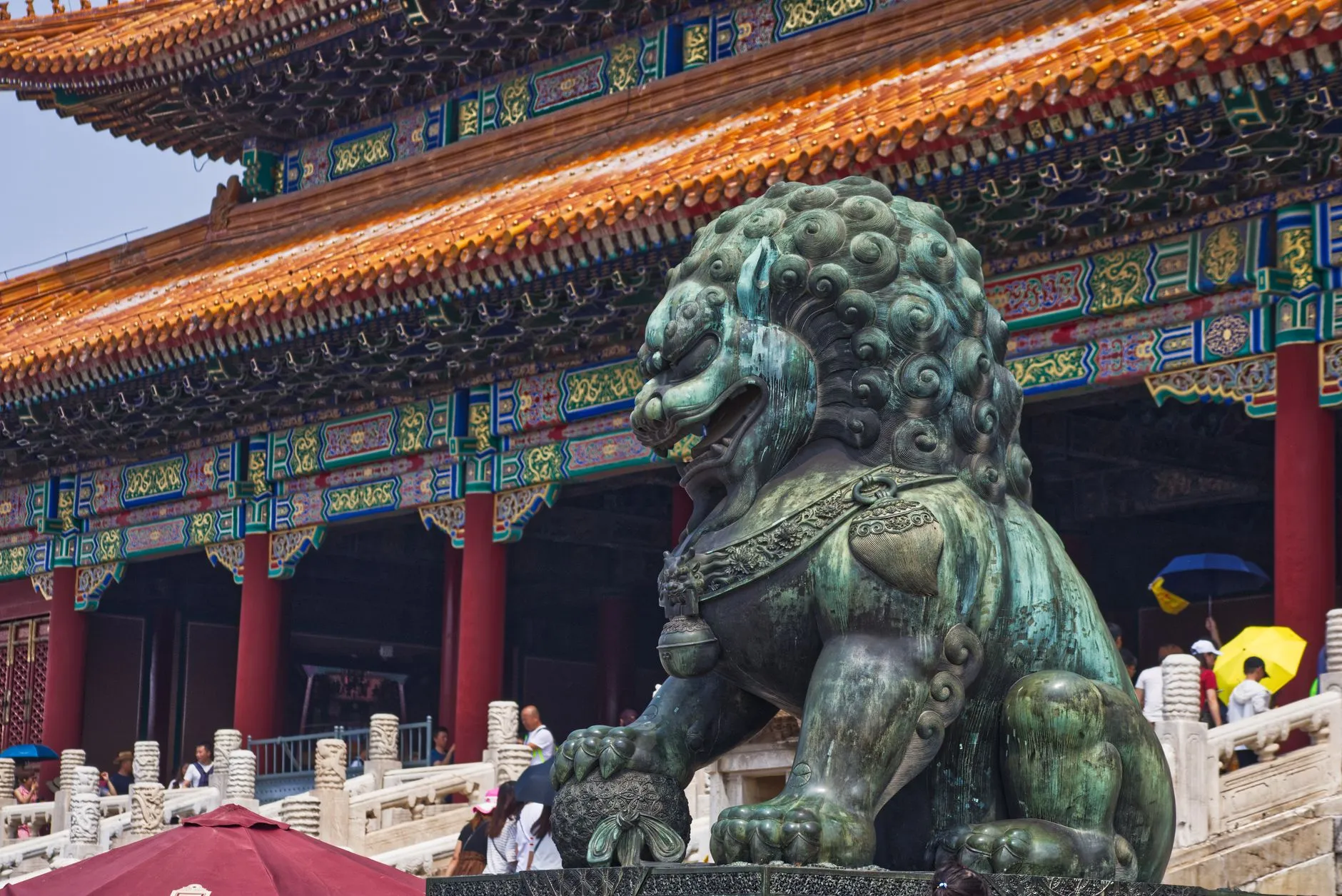 A bronze guardian lion at the Forbidden City, painted brackets and glazed roof tiles behind it