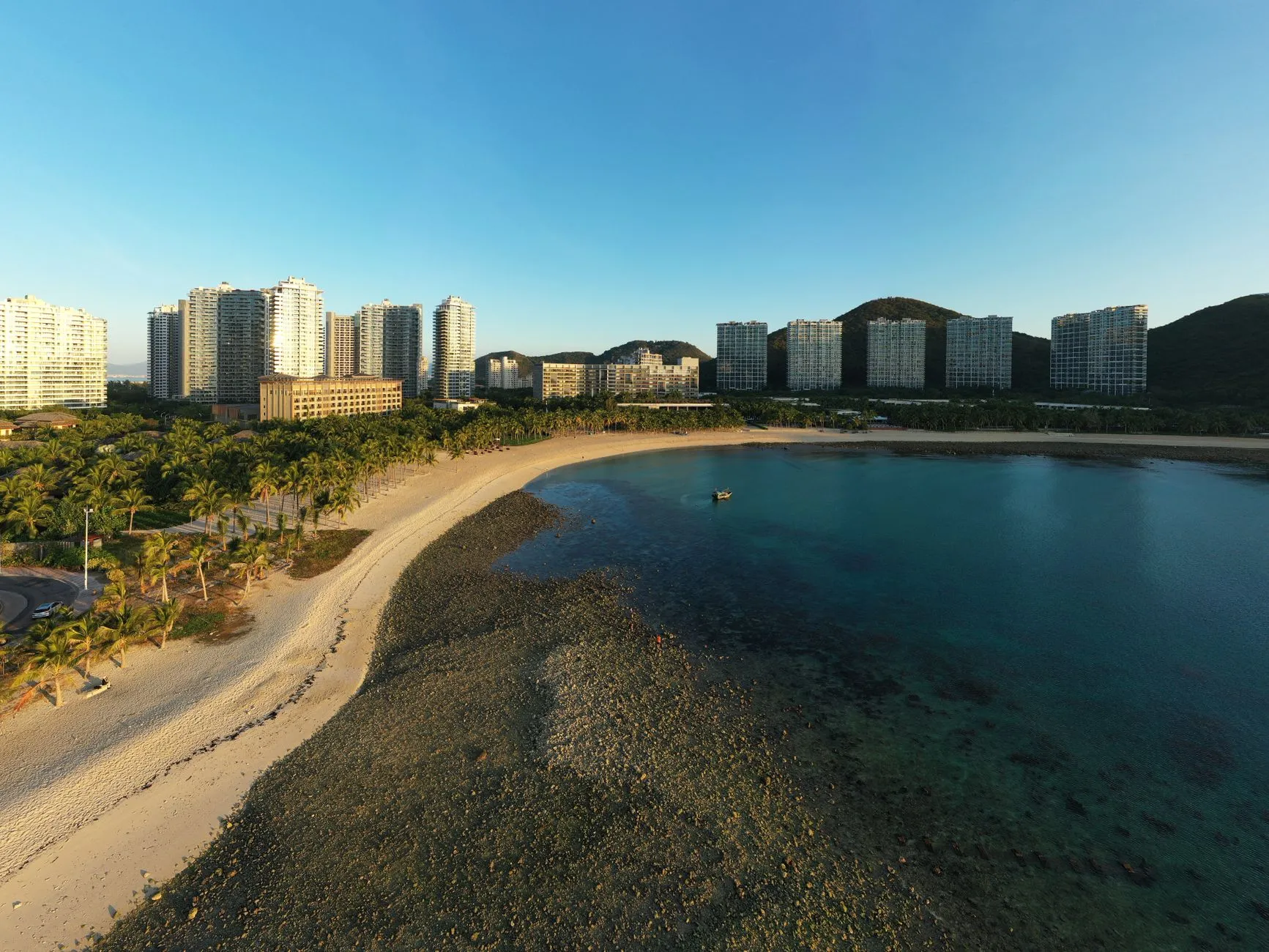 Aerial view of Sanya beachfront with palm trees and city skyline