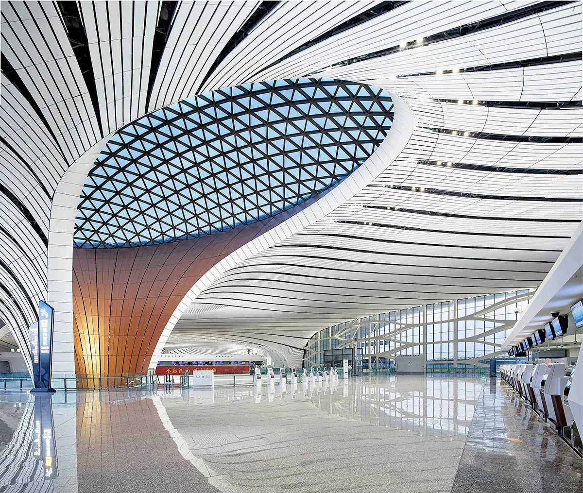 The interior of Beijing Daxing International Airport, showing the distinctive curved ribbed ceiling and central hub columns designed by Zaha Hadid