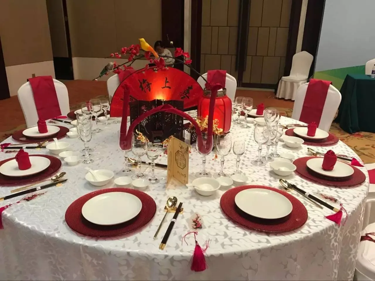 A round banquet table set with red plates, red-tasselled chopsticks and a folding screen