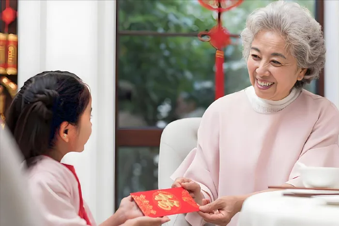 A grandmother handing a red envelope to a young child at Chinese New Year