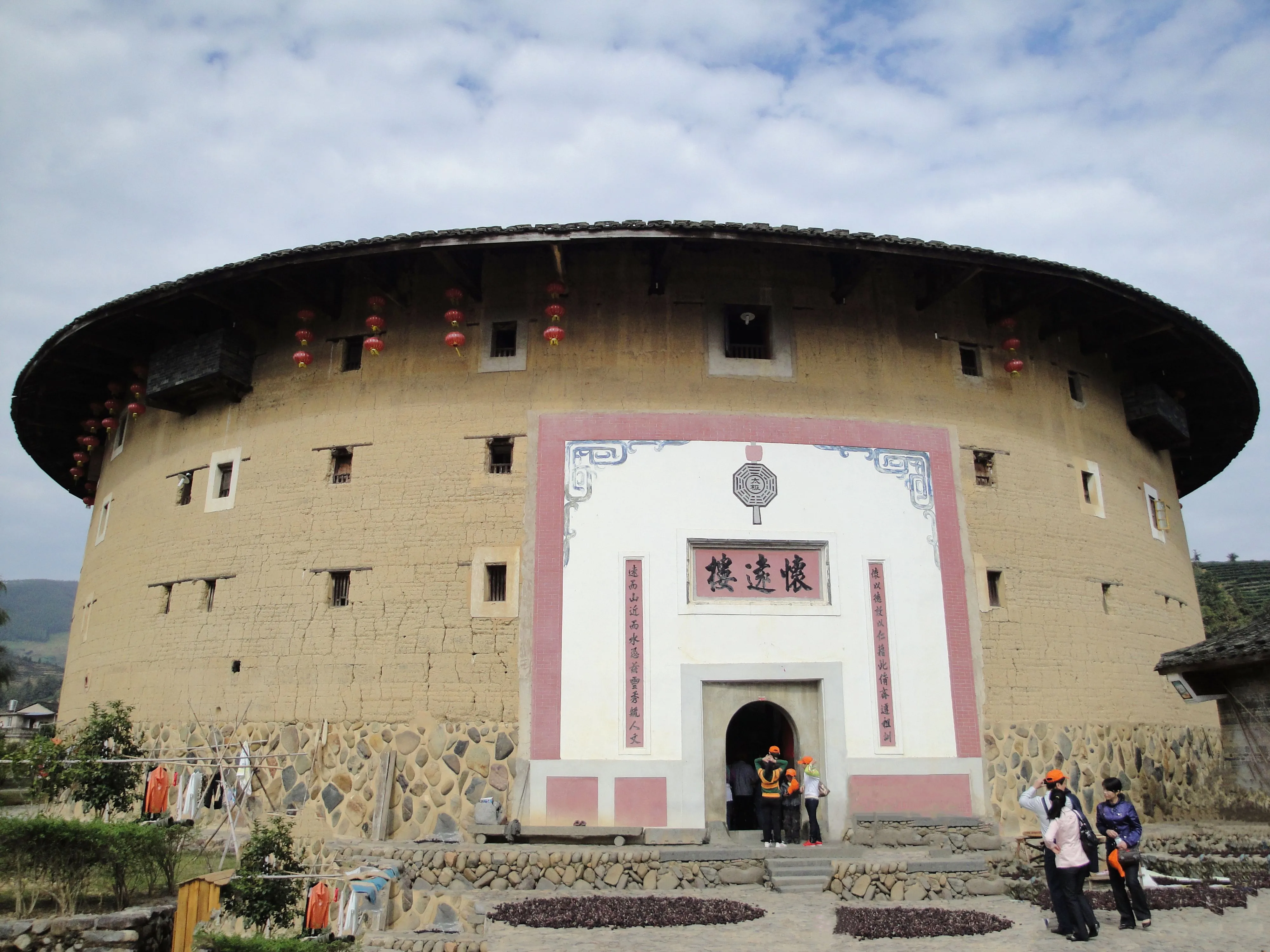 A giant circular rammed-earth tulou seen from outside, its name plaque reading Huaiyuan Lou