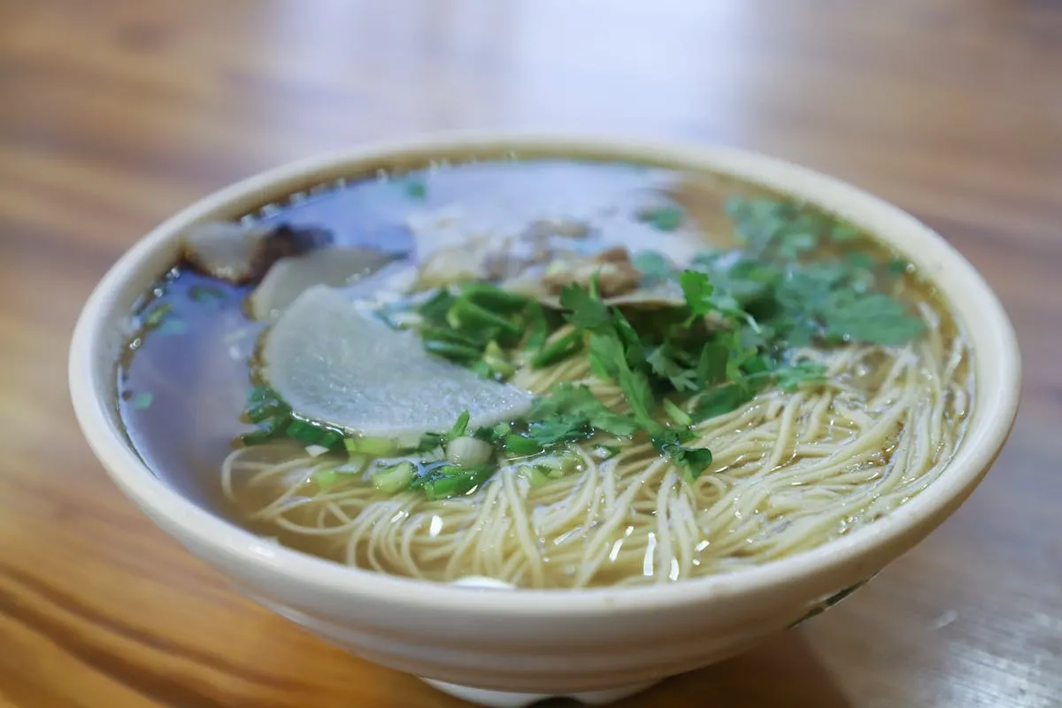 Warm noodle soup garnished with herbs and sliced radish in a ceramic bowl