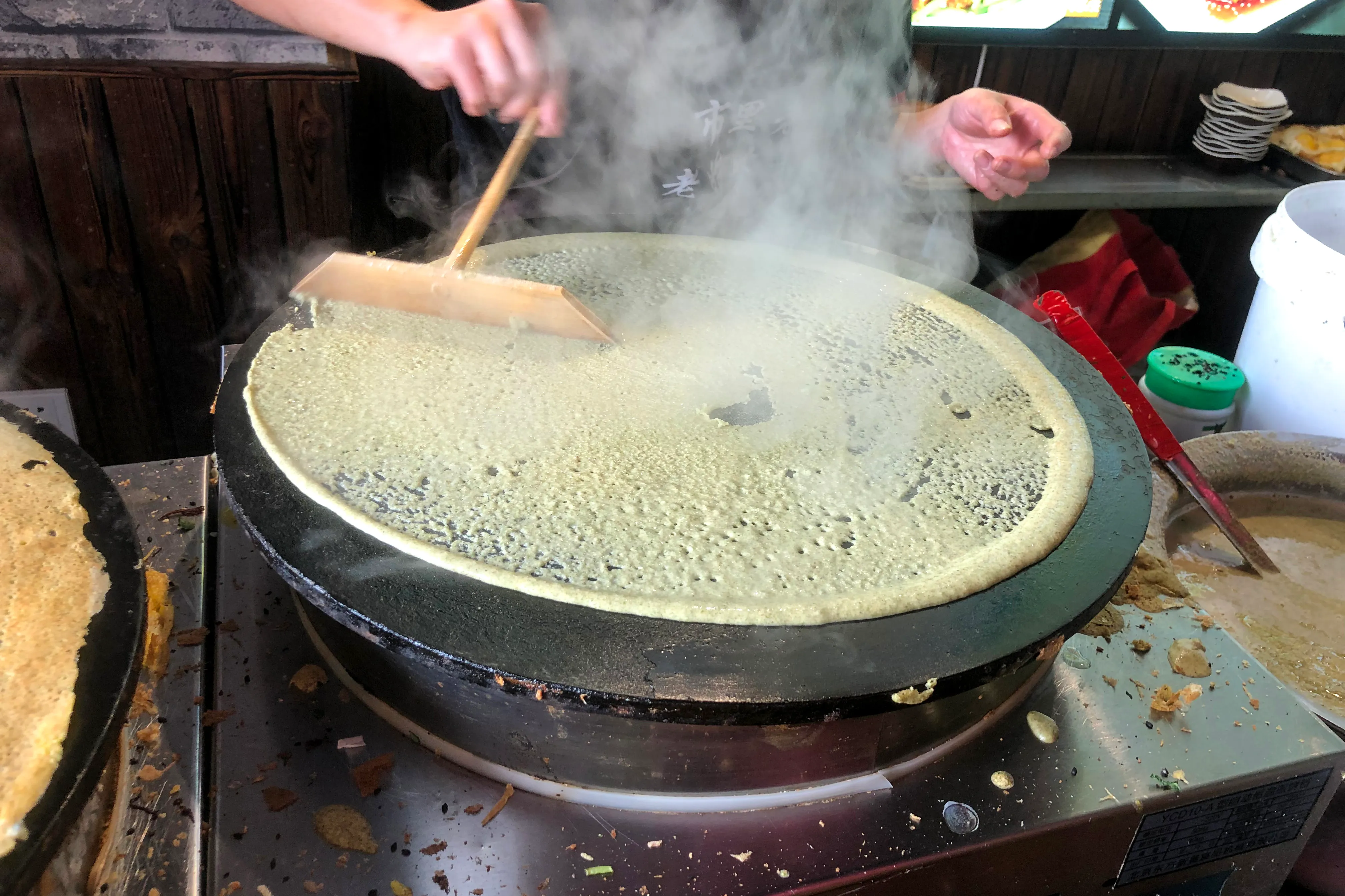 Street vendor making jianbing on a circular griddle in Tianjin