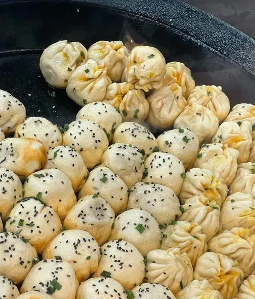 Shengjian Bao — pan-fried buns with golden crispy bottoms, scattered with sesame seeds and scallions